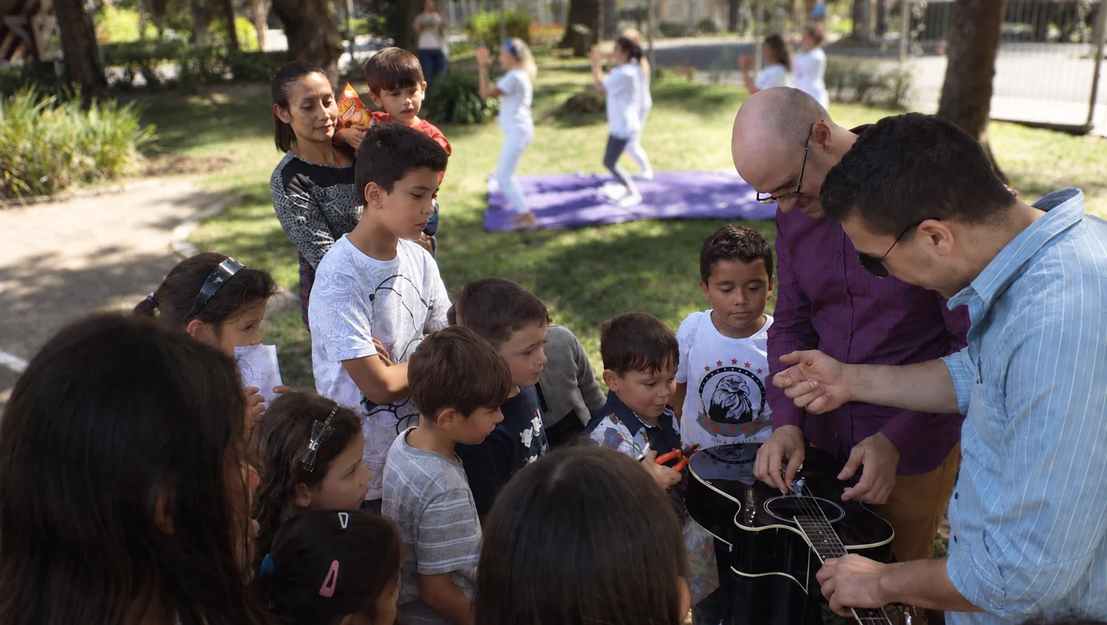 Professores apresentam o violão a um grupo de crianças em uma atividade ao ar livre.