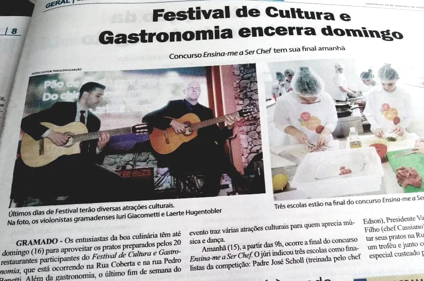 Recorte de jornal sobre o Festival de Cultura e Gastronomia, com apresentação dos violonistas Iuri Giacometti e Laerte Hugentobler.