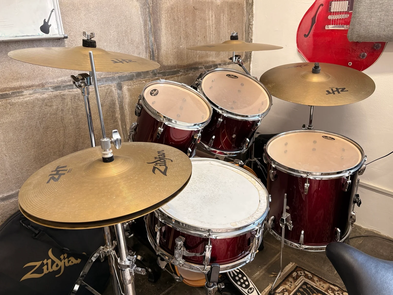 A bateria da Garage hoje, com tambores, pratos e uma guitarra vermelha ao fundo.