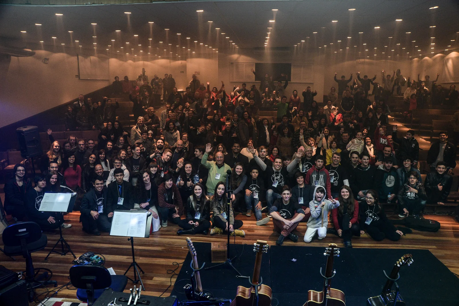 Alunos, professores e público reunidos no teatro, com instrumentos à frente, após o Guitar In Concert.